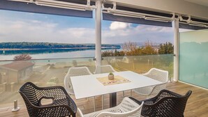 En balkon med et bord og stole, udsigt over en sø og fjerne træer.