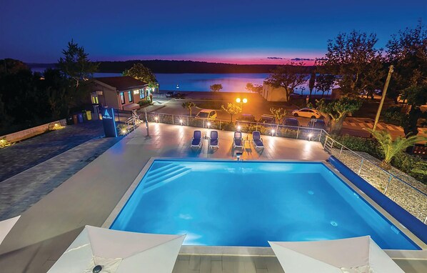 A swimming pool with lounge chairs and a view of the water at dusk. - 2 bedroom cozy apartment in Punat (Punat)