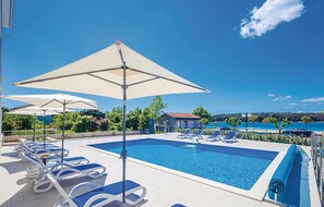 A swimming pool with lounge chairs and umbrellas, surrounded by greenery and a view of the sea. - 2 bedroom cozy apartment in Punat (Punat)
