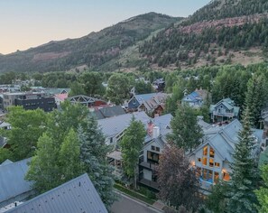 A residential area with houses surrounded by trees and hills in the background.