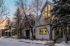 A residential building with a prominent front porch, a staircase leading to the entrance, and a snow-covered ground.