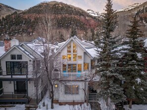 Une maison à plusieurs étages dotée d’un balcon, entourée d’arbres et de montagnes couverts de neige.