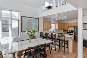 A spacious kitchen with a dining area, featuring a large island, wooden cabinets, and a view to the upper level.