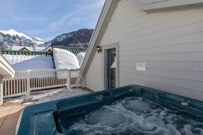 Un bain à remous sur un balcon avec vue sur les montagnes, des murs blancs et une clôture blanche.