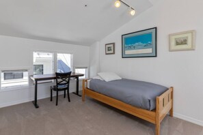 A bedroom with a bed, a desk, and a chair. There are windows and a ceiling light.