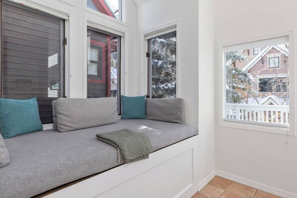 A room with a built-in bench seating area, a window with a view of a snowy landscape, and a white picket fence.