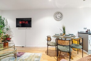 Ein modernes Wohnzimmer mit Essbereich, einem Flachbildfernseher, einer Wanduhr und einer Waschmaschine.