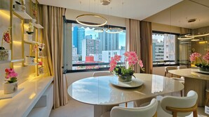 A modern dining area with a glass table, white chairs, and pink orchids. - Sofistica o na Gra a Calmaria a 5 min da Barra (Salvador)