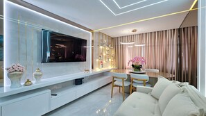A modern living room with a flat-screen TV, white sofas, a dining table, and decorative items. - Sofistica o na Gra a Calmaria a 5 min da Barra (Salvador)