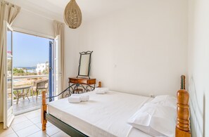 A bedroom with a bed, a dresser, a mirror, and a view of the outside. - Spacious modern sea view apartment: AC, walk to taverns and beaches (Aliki)