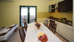 Een eetgedeelte met een tafel voor twee personen, een keuken met een fornuis en een gootsteen, en een schuifdeur naar een buitengebied.