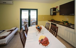 A dining area with a table set for two, a kitchen with a stove and sink, and a sliding glass door leading to an outdoor area. - 1 bedroom beautiful apartment in Drvenik (Drvenik)