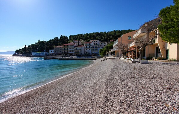 A pebble beach with buildings in the background. - Stunning apartment in Drvenik with house sea view (Drvenik)
