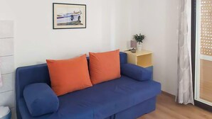 A blue sofa with orange cushions, a small plant on a side table, and a framed picture on the wall. - Cozy apartment in Zivogosce with WiFi (Zivogosce)