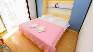 A neatly made bed with pink bedding and two folded towels, a bedside lamp, and a shelf with a lamp. - Cozy apartment in Zivogosce with WiFi (Zivogosce)