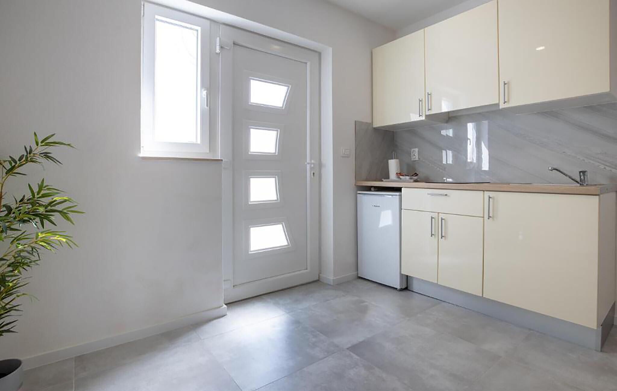 A modern kitchen with light-colored cabinets, a built-in dishwasher, and a marble backsplash.