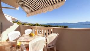 Un balcón con una mesa dispuesta para dos, sillas blancas y vistas al mar y las montañas.