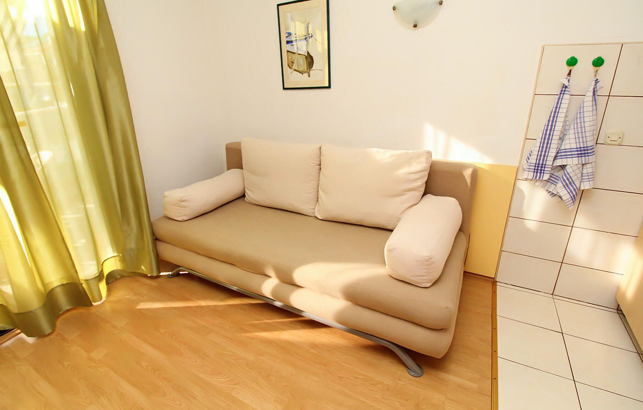 Quarto pequeno e moderno com sofá, cortina, luminária na parede e parede revestida com azulejos.
