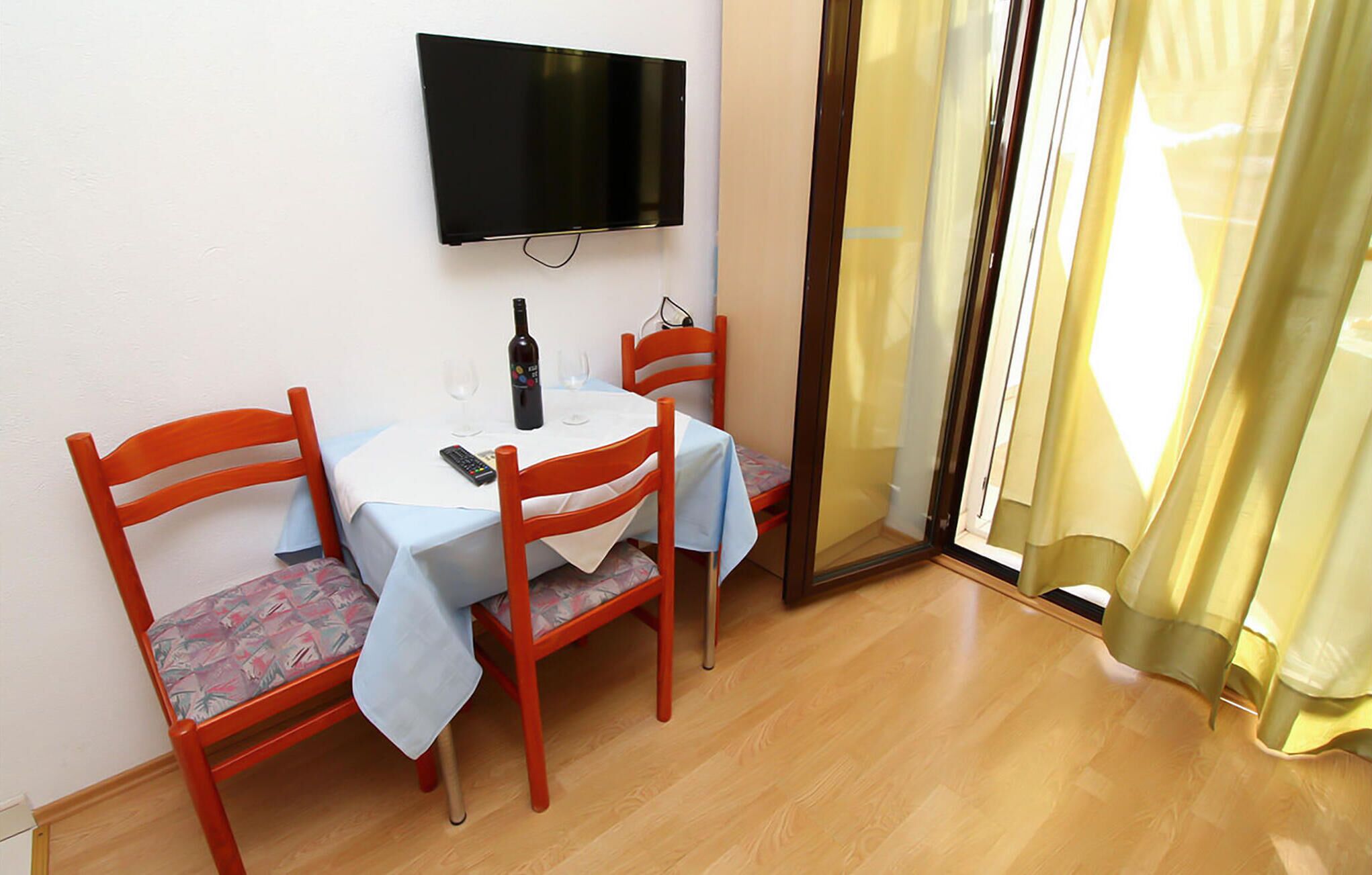 Un coin repas avec une table, des chaises, une bouteille de vin et un téléviseur fixé au mur.