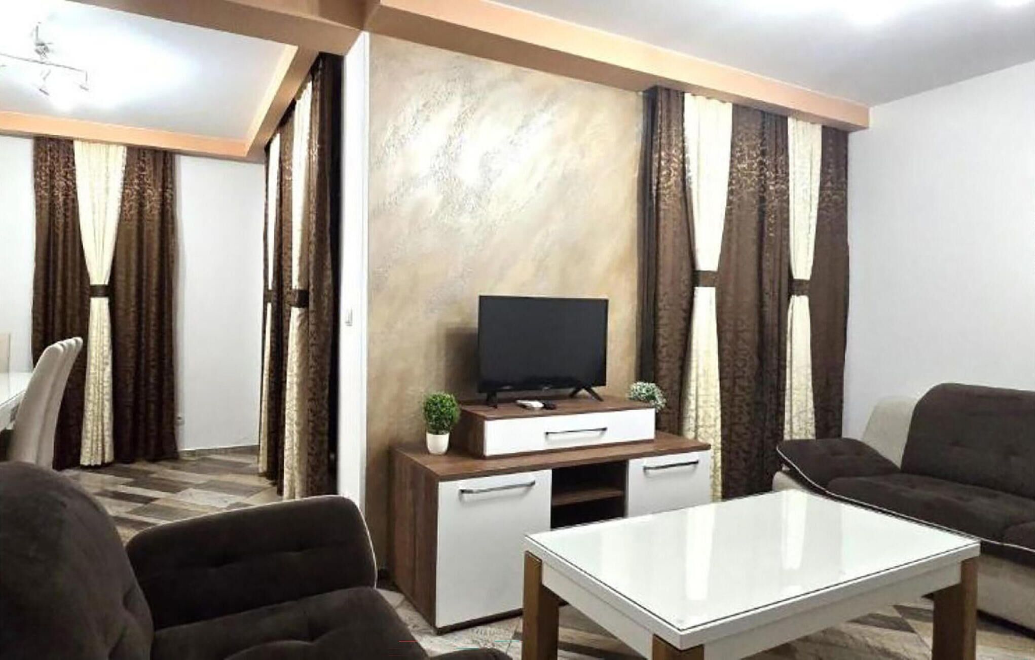 Een moderne woonkamer met een flatscreen televisie, een witte salontafel en twee banken.