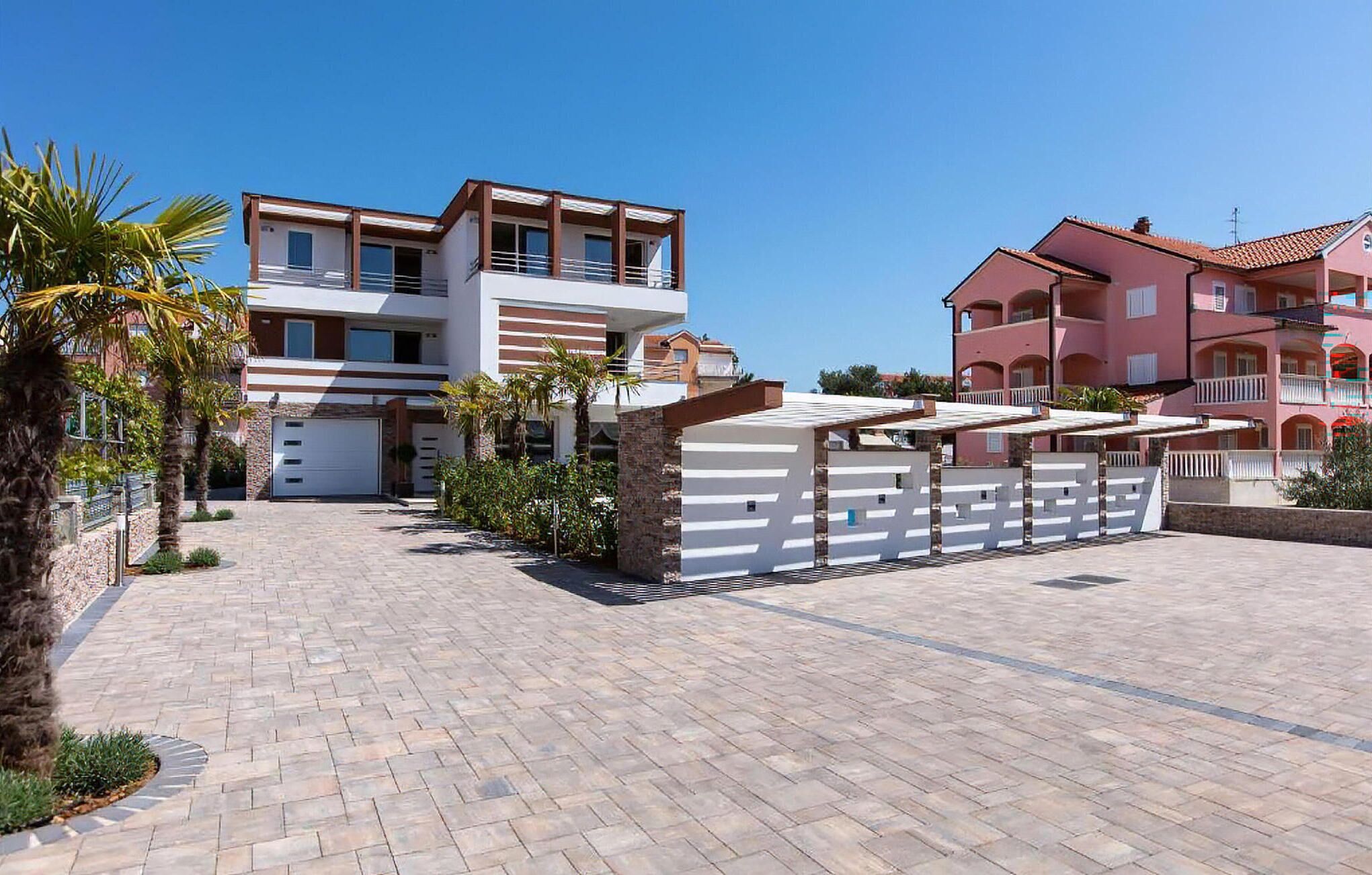 A modern multi-story residential building with a covered outdoor area and a paved driveway.