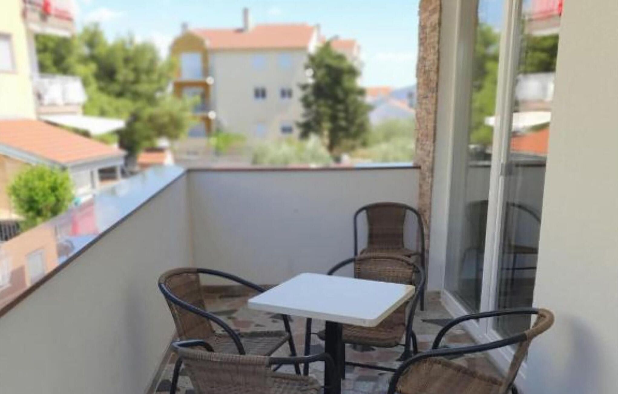 Ein Balkon mit Korbstühlen und einem kleinen Tisch, mit Blick auf ein Wohngebiet mit Häusern und Bäumen.