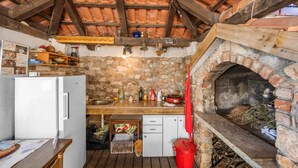 A rustic kitchen with a stone wall, wooden beams, a brick oven, and a refrigerator.