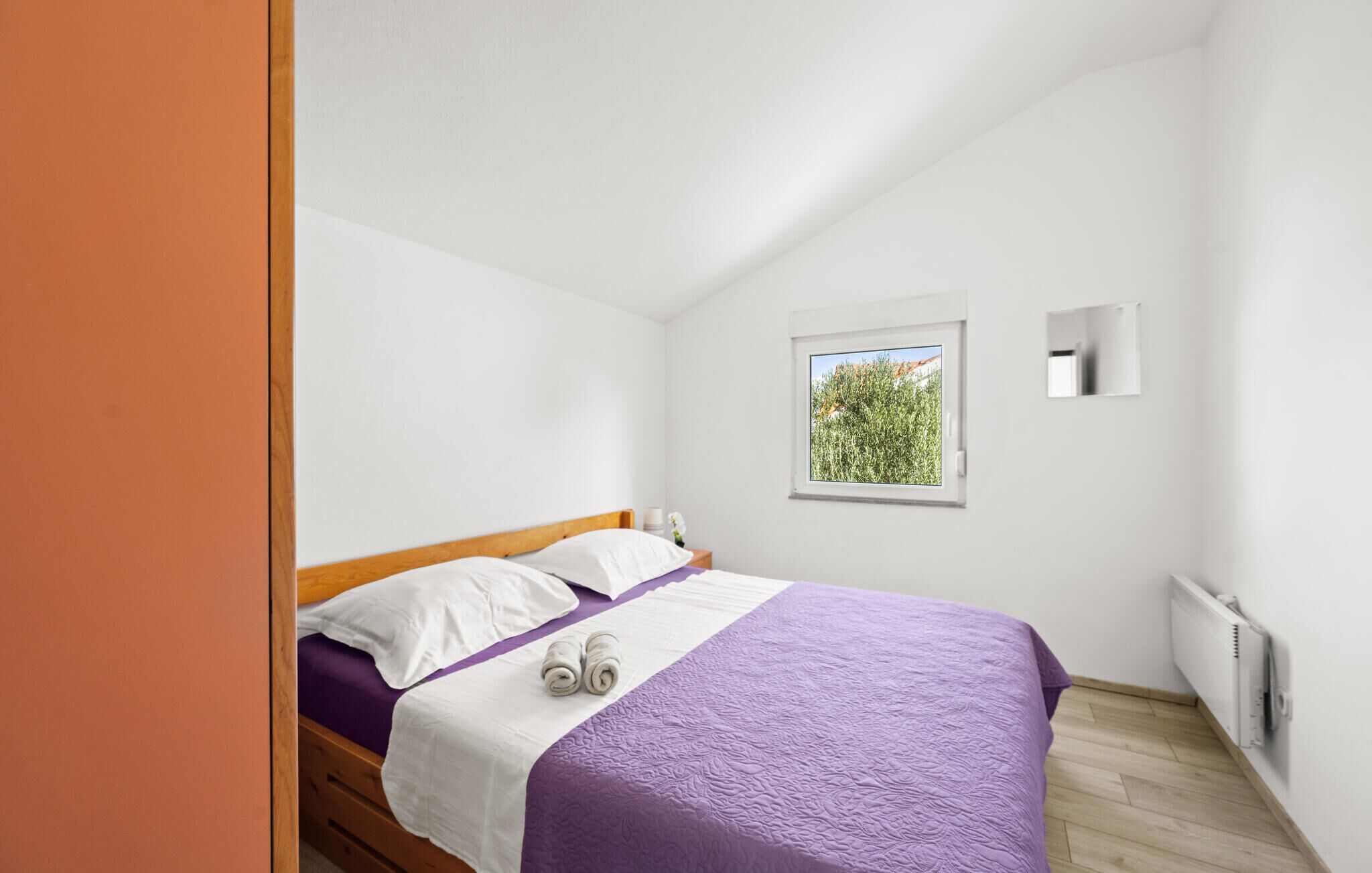 A bedroom with a bed, a window with a view, a wall-mounted light, and a radiator.