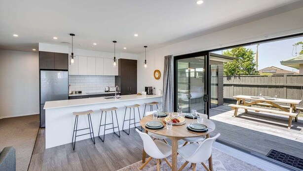 Una cocina moderna con una isla central, taburetes de bar y una mesa de comedor para cuatro.