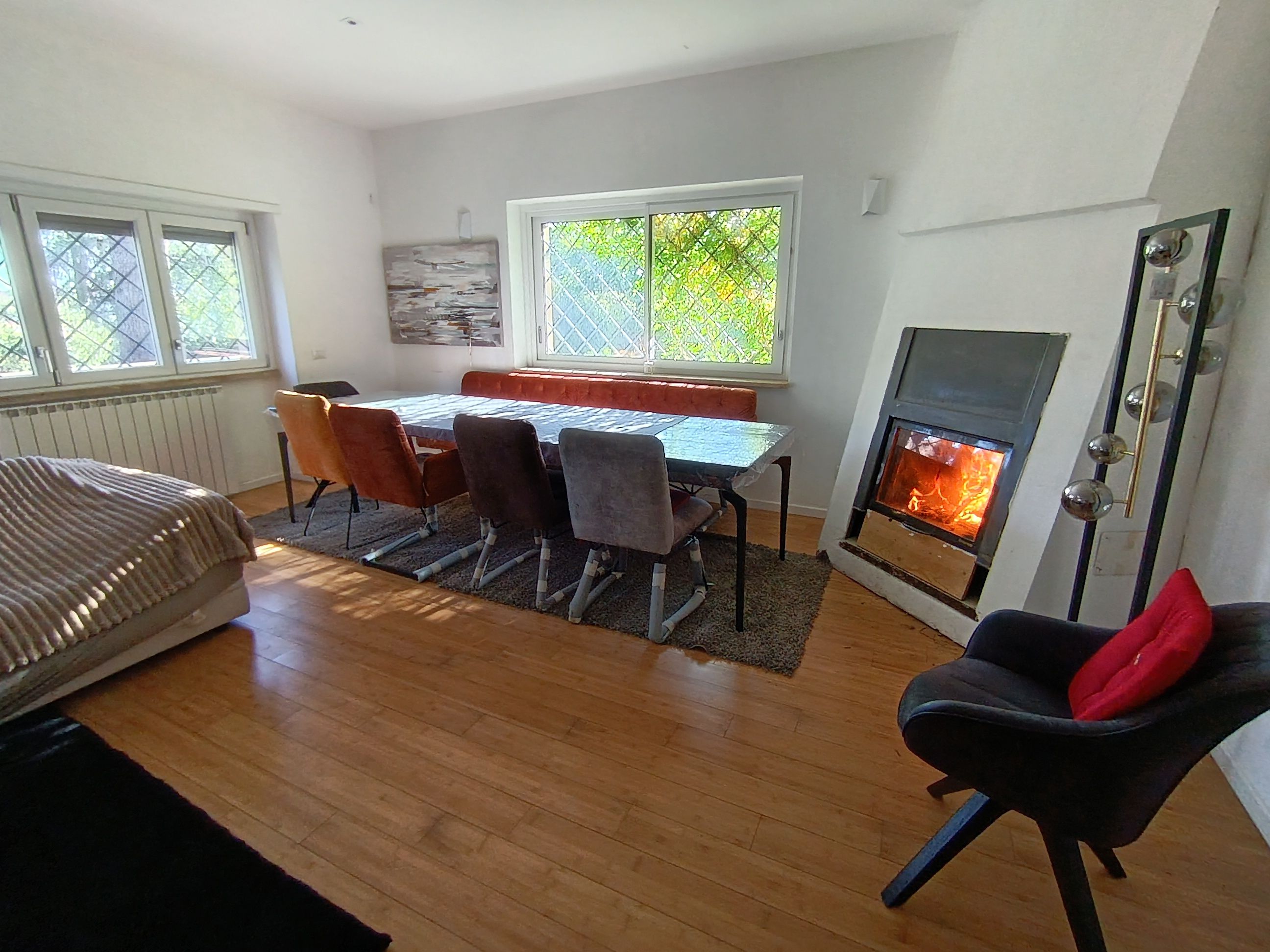 Ein Zimmer mit Esstisch, Stühlen, einer Couch, einem Kamin und einem Fenster mit Blick ins Grüne.