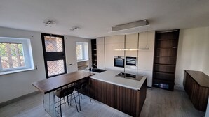 A modern kitchen with a central island, built-in oven, and a window overlooking a courtyard.