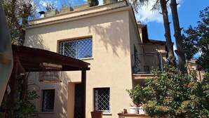 A two-story building with a beige exterior, a covered patio area, and a small garden with potted plants.
