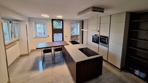 A modern kitchen with a central island, two bar stools, a built-in oven, and a window with a view.