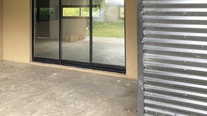 Un patio cubierto con una puerta corrediza de vidrio que da a un jardín trasero.