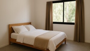 Una cama individual con estructura de madera y ropa de cama blanca, ubicada junto a una ventana con cortinas marrones.