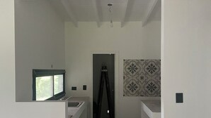 Un pasillo estrecho con una zona de cocina a la izquierda, una escalera en el centro y un papel tapiz decorado a la derecha.