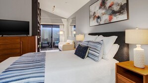Moderni hotellihuone, jossa on suuri sänky, taulutelevisio, parveke istuimineen sekä suuri abstrakti maalaus.