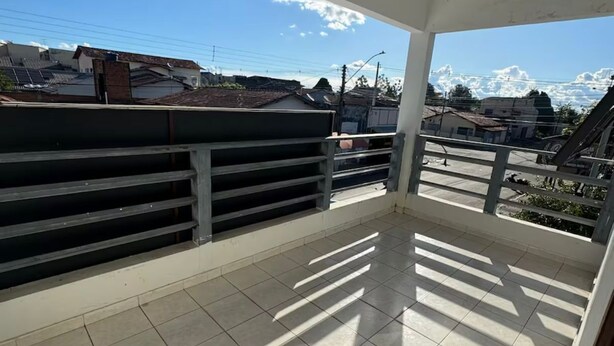 Ein überdachter Balkon mit Fliesenboden, Metallgeländern und Blick auf Gebäude und einen klaren Himmel.