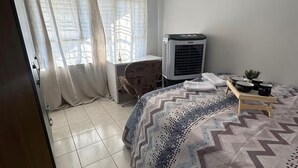 Ein Schlafzimmer mit einem Bett, einer Klimaanlage, einem Sessel und einem kleinen Tisch mit Gegenständen darauf.