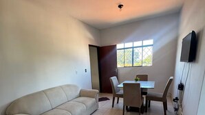 Ein Wohnzimmer mit einem beigen Sofa, einem Esstisch mit Stühlen und einem an der Wand montierten Fernseher.