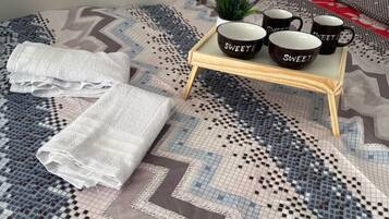 A bed with a patterned bedspread, a tray with mugs, and folded towels.