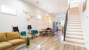 Ein modernes Wohnzimmer mit einer Couch, einem Couchtisch und einem Essbereich mit Stühlen. Eine Treppe führt zu einer weiteren Ebene.