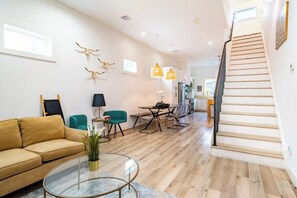 Een moderne woonkamer met een bank, een salontafel en een eethoek met stoelen. Er is een trap die naar een ander niveau leidt.