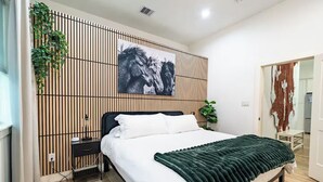 Ein modernes Schlafzimmer mit Bett, Wandbild, Nachttisch und Steckdose.
