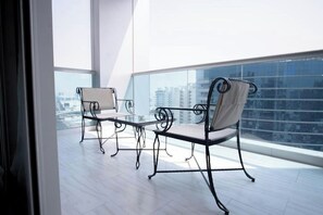 A balcony with two chairs and a table, large windows, and a city view. - Jood Hotel Apartments (Dubai)