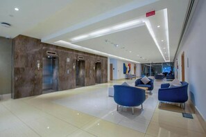 Una hall moderna con un design pulito e spazioso, che include un'area salotto centrale con poltrone blu e pavimento piastrellato.