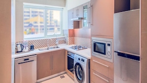 A modern kitchen with stainless steel appliances, a washing machine, and a large window providing natural light.