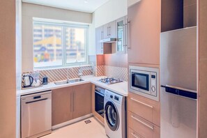 Una cocina moderna con electrodomésticos de acero inoxidable, lavadora y un amplio ventanal que proporciona luz natural.