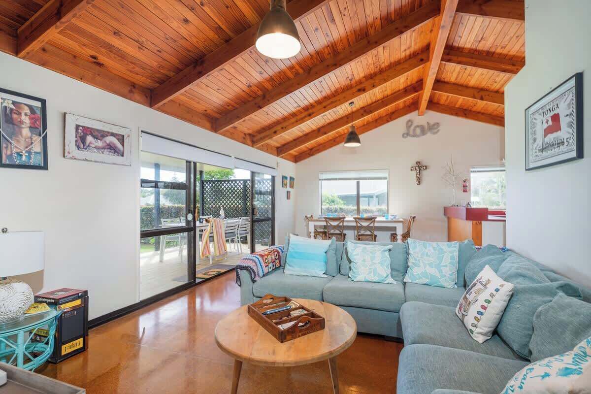 A cozy living room with a wooden ceiling, a sofa, a coffee table, and a dining area with a cross on the wall.