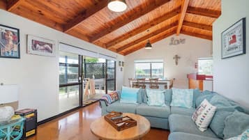A cozy living room with a wooden ceiling, a sofa, a coffee table, and a dining area with a cross on the wall.